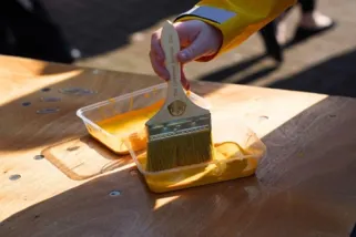 A hand holding a paint brush over a yellow paint container

AI-generated content may be incorrect.